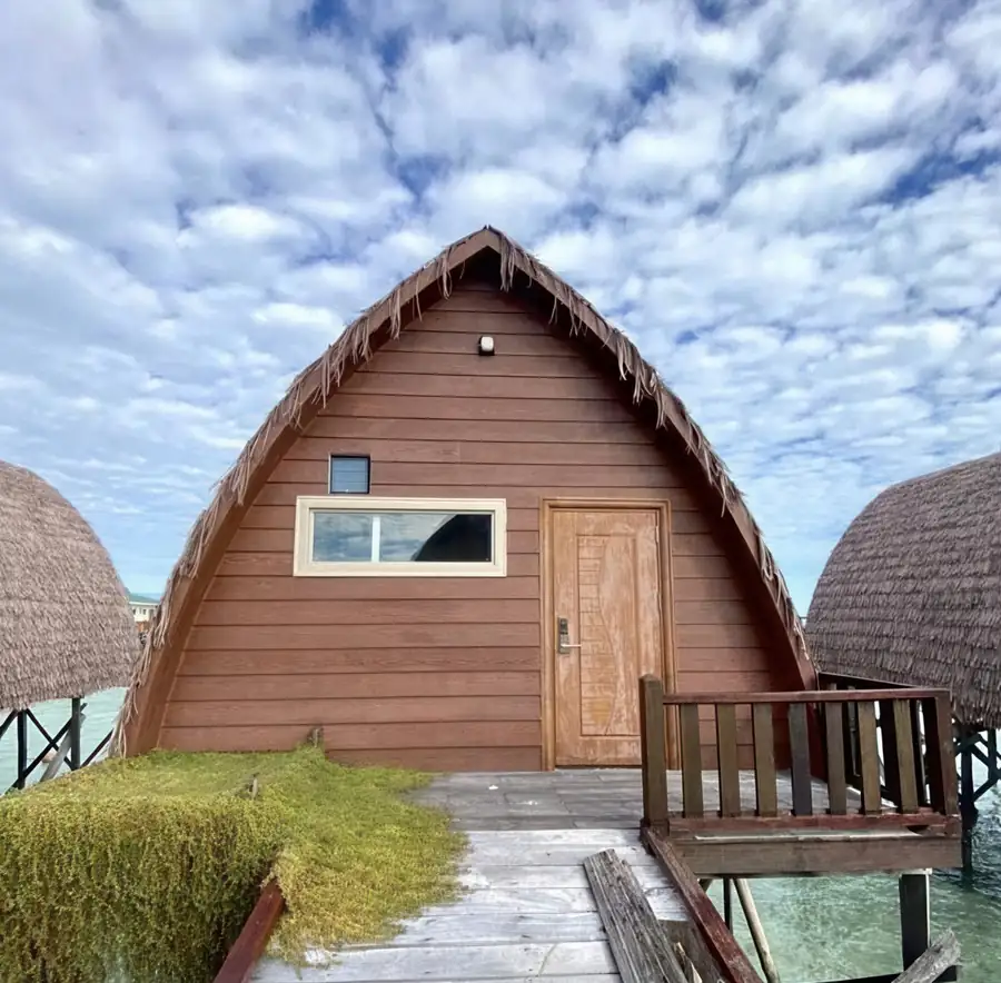 A timber-clad chalet with a traditional Sabah style pointed roof with thatched trim and wooden entrance door at Crystal Resort